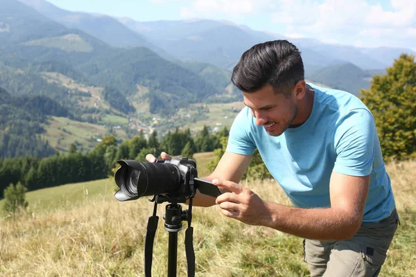 三脚の上で現代的なカメラで山の風景の写真を撮る男屋外 — ストック写真