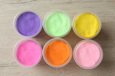 Plastic containers with colorful play dough on white wooden background, flat lay