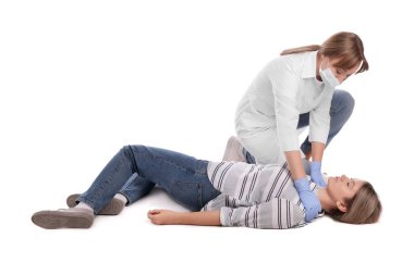 Üniformalı ve koruyucu maskeli bir doktor beyaz arka planda baygın bir kadına ilk yardım yapıyor.