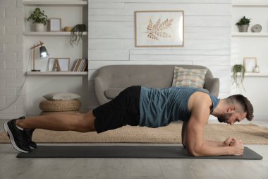 Yakışıklı adam evde yoga minderi üzerinde kalas egzersizi yapıyor.