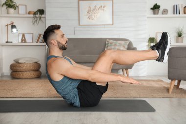 Evdeki yoga minderinde karın kası egzersizi yapan yakışıklı adam.
