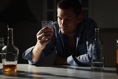 Mutfaktaki masada alkollü içeceği olan bağımlı bir adam.