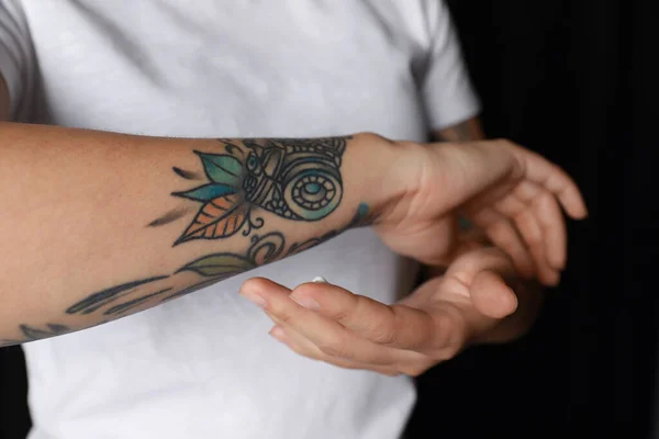 Donna Che Applica Crema Sul Braccio Con Tatuaggi Sfondo Nero — Foto Stock