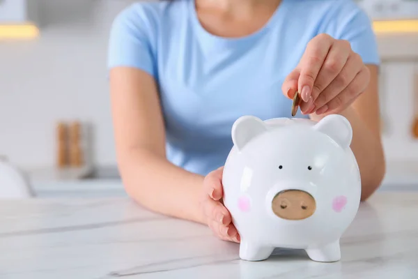 Young Woman Putting Coin Piggy Bank Table Indoors Closeup Space — стоковое фото