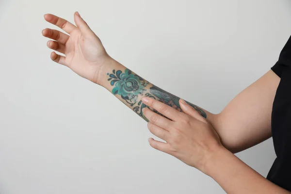 Mulher Aplicando Creme Seu Braço Com Tatuagens Contra Fundo Claro — Fotografia de Stock
