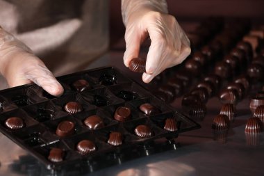 Kadın üretim bandında nefis şekerlemeler paketliyor, yakın plan.