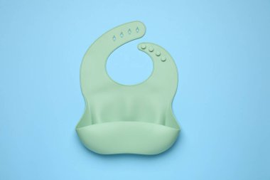 Green silicone baby bib on light blue background, top view. First food