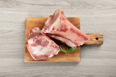 Cutting board with raw chopped meaty bones and basil on wooden table, top view
