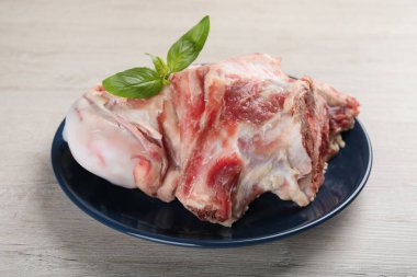 Plate with raw chopped meaty bones and basil on white wooden table