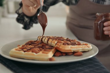 Lezzetli Belçika wafflelarını beyaz tezgahta çikolatalı kremayla süsleyen kadın, yakın plan.