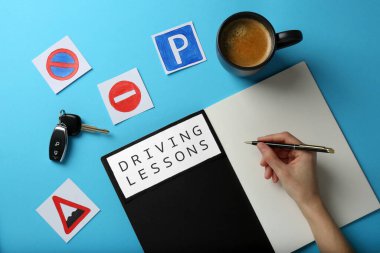 Woman with workbook for driving lessons on light blue background, top view. Passing license exam