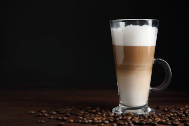 Lezzetli latte macchiato ve kahve çekirdekleri ahşap masada, mesaj için yer var.