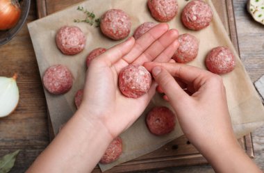 Woman making fresh raw meatballs at wooden table, top view