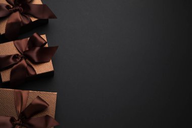 Brown gift boxes decorated with satin bows on black background, flat lay. Space for text