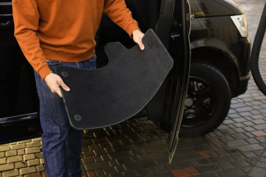 Man taking carpets from auto for cleaning at self-service car wash, closeup