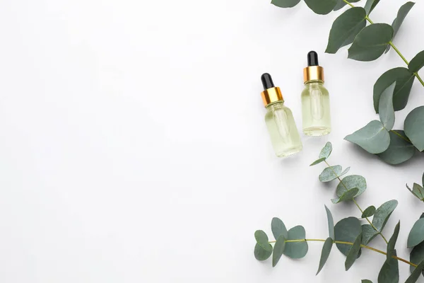 Bottles of eucalyptus essential oil and plant branches on white background, flat lay. Space for text