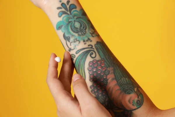 Mujer Aplicando Crema Brazo Con Tatuajes Sobre Fondo Amarillo Primer —  Fotos de Stock