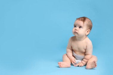 Açık mavi arka planda oturan bebek bezi takmış şirin bir bebek. Metin için boşluk