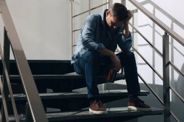 Alkollü içkisi olan bağımlı bir adam içeride merdivenlerde içki içiyor. Metin için boşluk