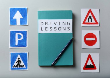 Açık gri arka planda sürüş dersleri ve yol işaretleri için çalışma kitabıyla düz kompozisyon. Ehliyet sınavını geçmek