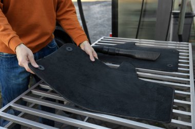 Otomobil halısı olan adam oto yıkamada elektrikli süpürgenin yanında, yakın plan.