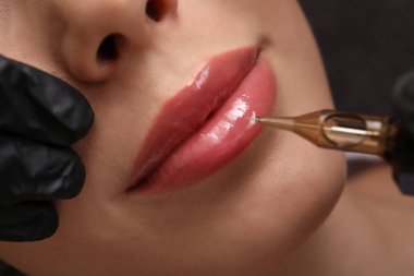 Dövme salonunda kalıcı olarak dudak makyajı yaptıran genç bir kadın.