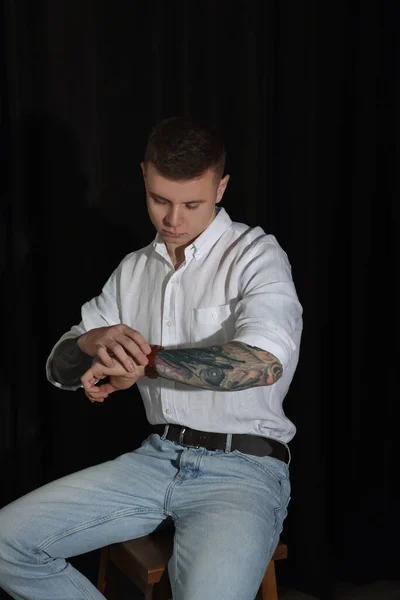 Ung Man Med Tatueringar Och Armbandsur Sitter Pall Mot Mörk — Stockfoto