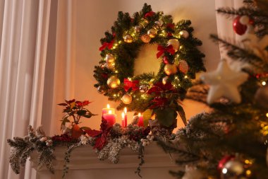 Beyaz duvardaki güzel Noel çelengi dekore edilmiş şömine rafının üzerinde.