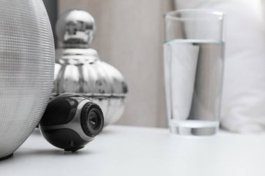 Yatak odasındaki beyaz komodinin üzerinde küçük gizli kamera.