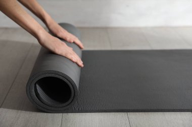 Kadın siyah yoga minderi yuvarlıyor. Kapalı bir yerde, yakın plan.