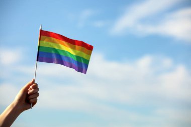 Mavi gökyüzüne karşı parlak LGBT bayrağı tutan kadın, yakın plan. Metin için boşluk