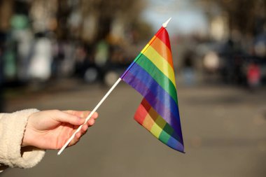 Şehir caddesinde elinde parlak LGBT bayrağı tutan kadın, yakın plan.