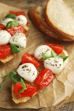 Mozzarella 'lı lezzetli sandviçler, taze domates ve parşömen üzerine fesleğen.