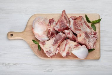 Beyaz ahşap masa üzerinde çiğ et ve fesleğen ile tahta kesme, üst görünüm