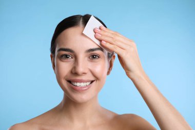 Açık mavi arkaplanda matlaştırıcı mendil kullanan güzel bir kadın