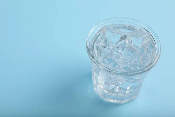 Glass of soda water with ice on light blue background. Space for text