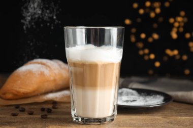 Lezzetli latte macchiato, kruvasan ve kahve çekirdekleri ahşap masada.
