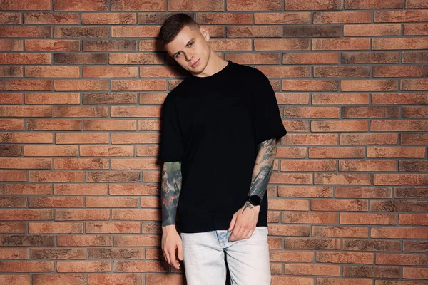 Young man with tattoos near brick wall