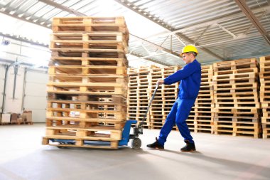Depoda manuel forkliftle ahşap paletler taşıyan bir işçi.