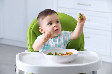Evdeki yüksek sandalyede sağlıklı yiyecekler yiyen şirin bir bebek.