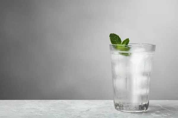 Glass of soda water with ice and mint on grey table. Space for text