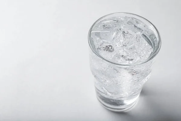 Glass of soda water with ice on light background. Space for text