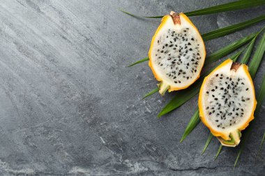 Lezzetli kesilmiş ejderha meyvesi (pitahaya) ve gri masa üzerinde tropikal yaprak, düz yatıyordu. Metin için boşluk