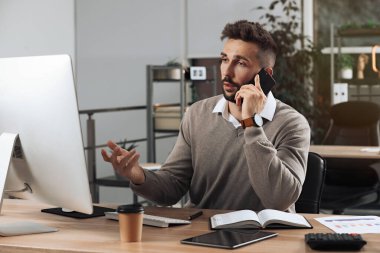 Ofiste çalışırken telefonla konuşan bir adam.