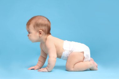 Açık mavi arka planda emekleyen bezli şirin bir bebek.