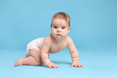 Açık mavi arka planda emekleyen bezli şirin bir bebek.