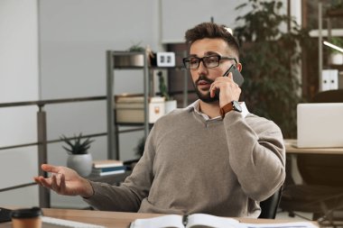 Ofiste çalışırken telefonla konuşan bir adam.