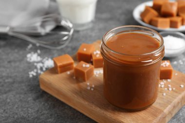 Cam kavanozda lezzetli tuzlu karamel ve gri masada şeker, metin için yer var.