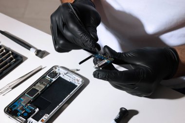 Teknisyen, beyaz masada bozuk akıllı telefonu tamir ediyor.