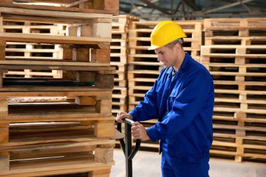 Depoda manuel forkliftle ahşap paletler taşıyan bir işçi.